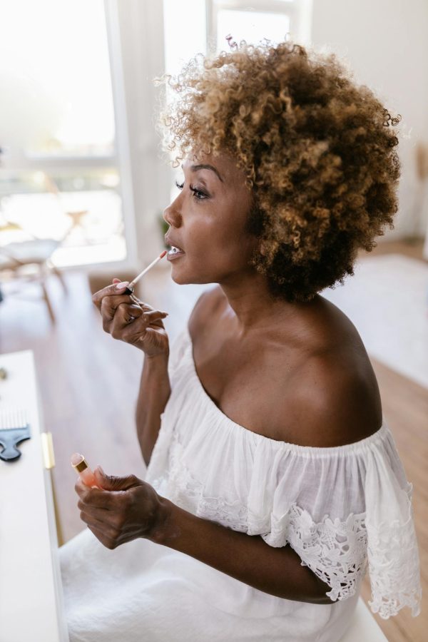 Elegant African American woman applying lip gloss indoors, embracing beauty and self-care with grace.